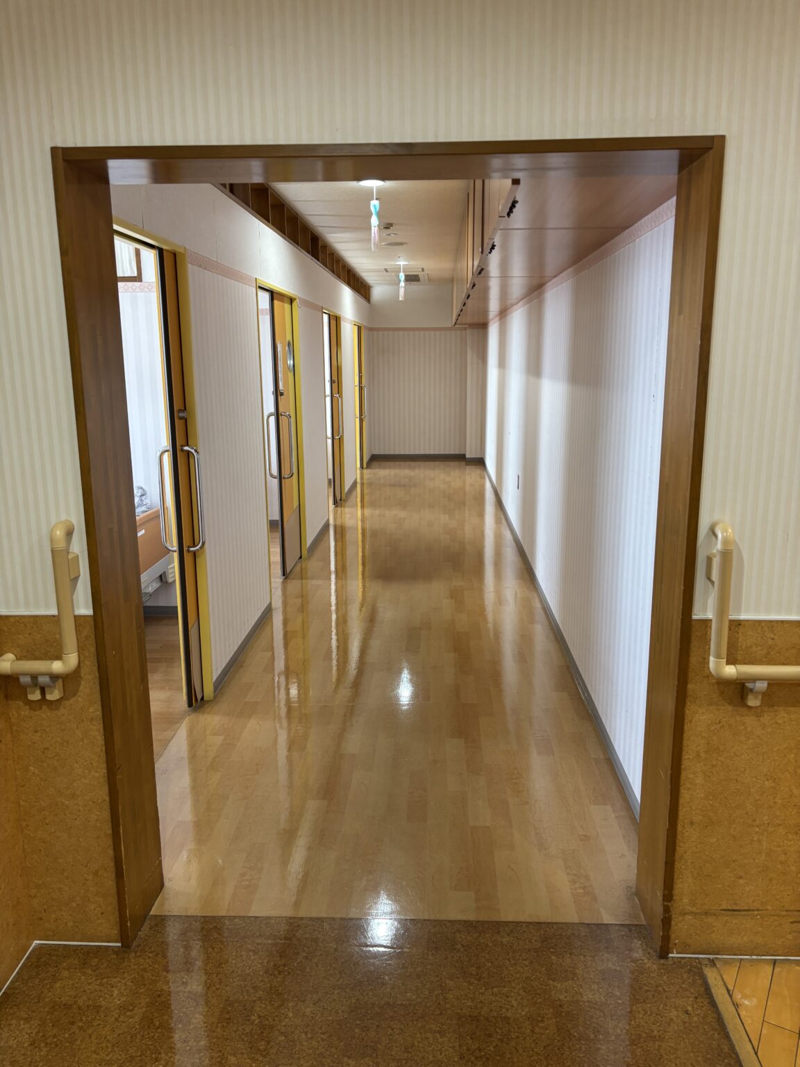 居室廊下。複数の個室ドアが並び、清潔で明るい共有通路。