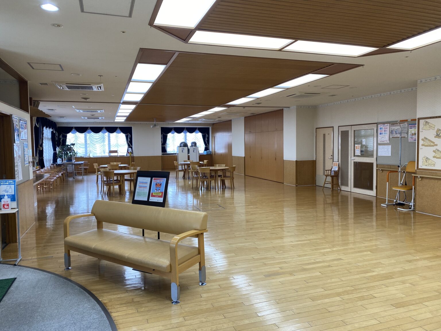 明るい共用スペース。木製の天井、広々とした床、ベンチと食卓が配置された多目的ホール
