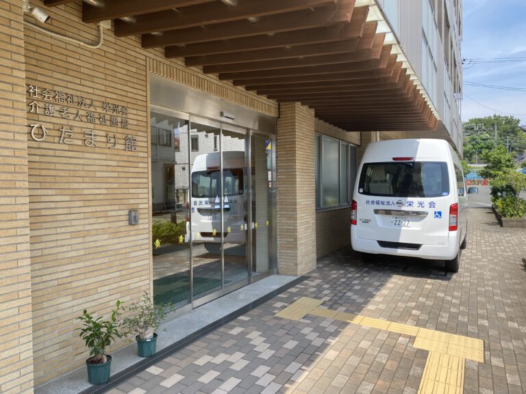 介護施設の玄関と車寄せ。送迎車が駐車されており、施設入口が確認できます。